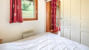 Une chambre à coucher avec un lit, une fenêtre avec des rideaux, un radiateur et une porte donnant sur l’extérieur.