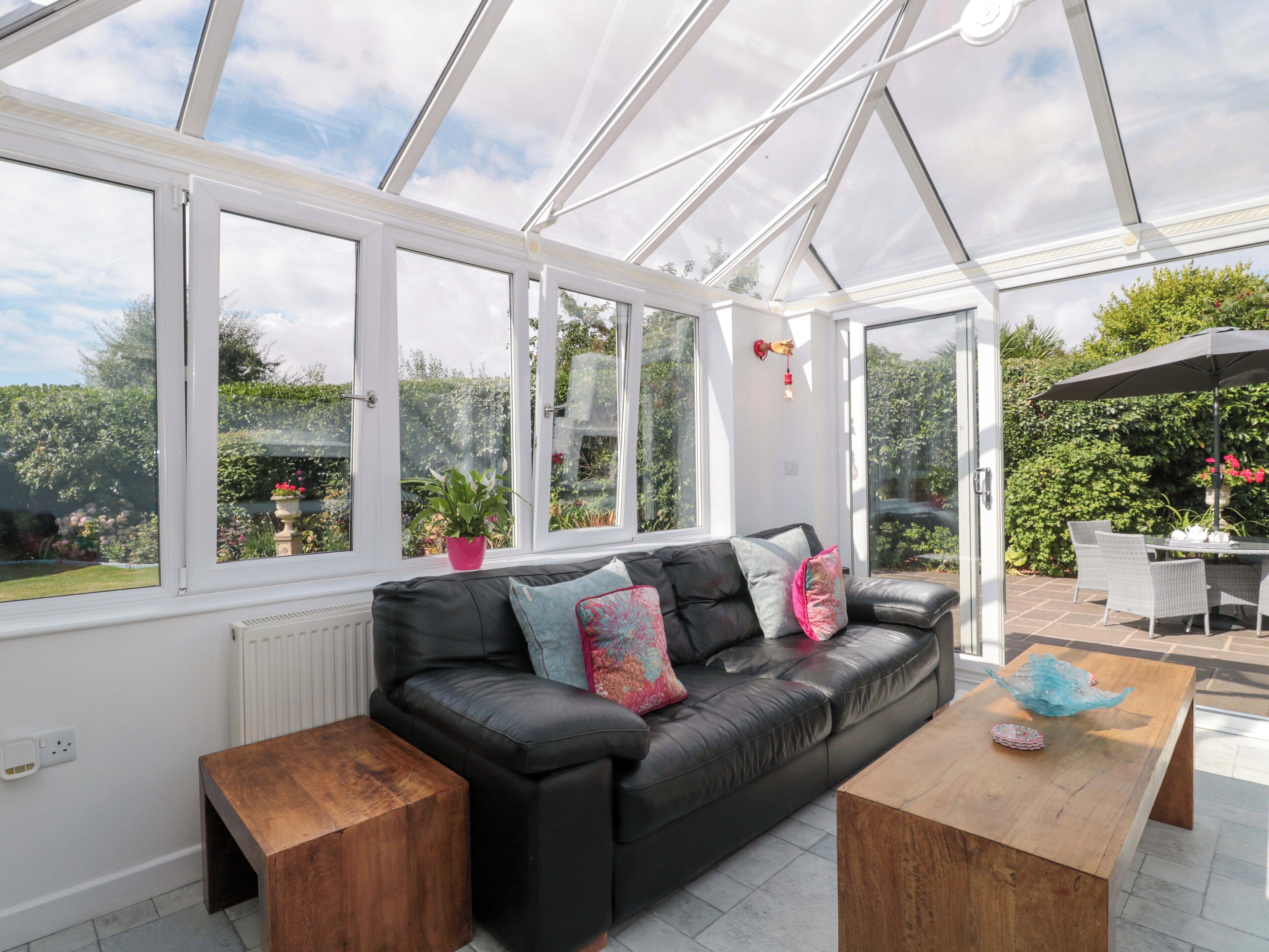 A conservatory with a black leather sofa, wooden side tables, and a wooden coffee table.