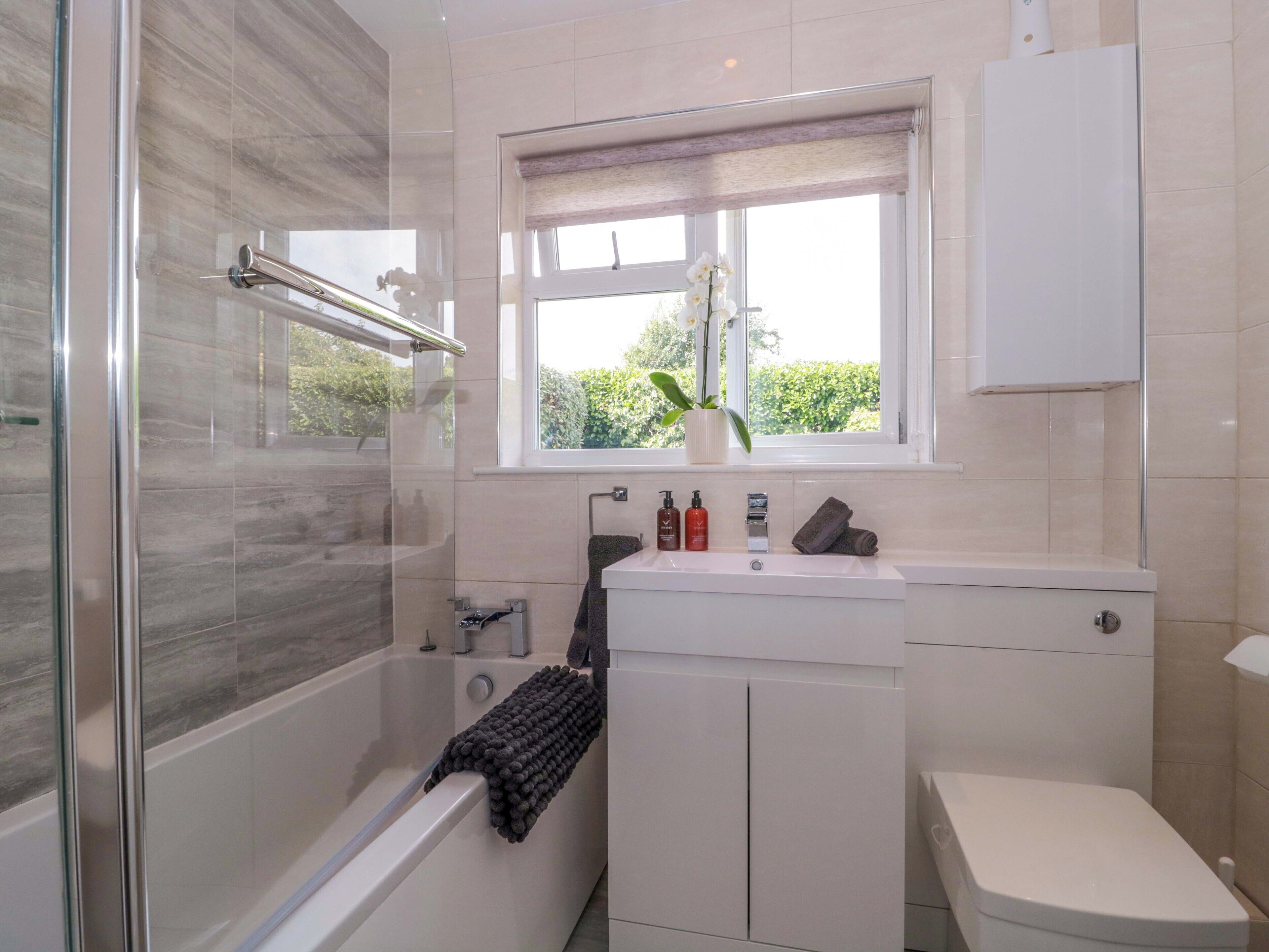 Une salle de bain moderne dotée d’une douche à parois de verre, d’une baignoire, de toilettes et d’une fenêtre donnant sur un paysage verdoyant.