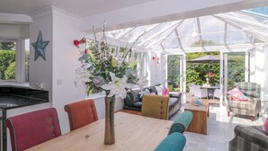 A spacious living area with a wooden dining table, a sofa, and a glass-enclosed patio.