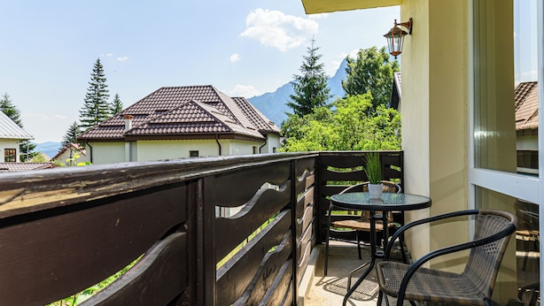 A balcony with a wooden railing, a round table with chairs, and a view of houses and mountains in the background. - Tranquil 1-bedroom house in Bușteni (Bușteni)