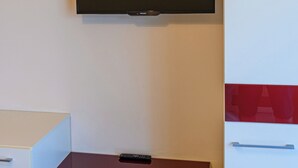 A room with a flat-screen TV mounted on the wall, a white cabinet with drawers, and a red countertop. - Tranquil 1-bedroom house in Bușteni (Bușteni)