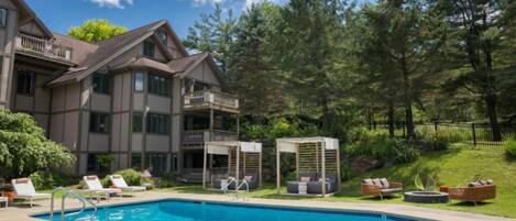 A hotel with a swimming pool, outdoor seating, and a forested area.