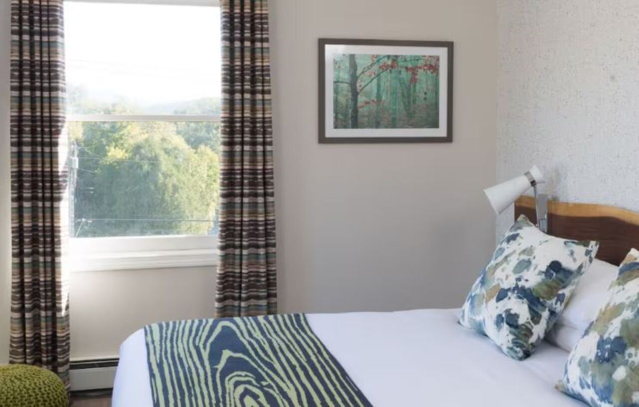 Une chambre d’hôtel avec un lit, une fenêtre avec des rideaux, un tableau encadré au mur et une lampe de chevet.