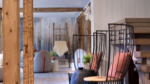 A cozy room with a wooden ceiling, a sofa, and a chair with a unique wireframe design. - Enjoy Nature & Town | Stay in Style at Field Guide Lodge, Close to Everything (Stowe)