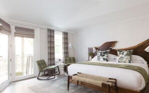 A bedroom with a large bed, two chairs, a small table, and a view of the outdoors through a sliding door. - Scenic Lodge in Town | Hike, Dine & Relax All Within Walking Distance (Stowe)