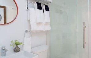 A modern bathroom with a glass shower enclosure, a toilet, a sink with a vase of flowers, and a mirror with a red frame. - Scenic Lodge in Town | Hike, Dine & Relax All Within Walking Distance (Stowe)