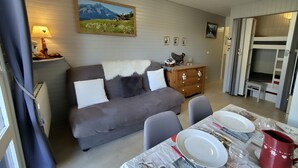 Zona d'estar acollidora amb un sofà, una taula de dinar preparada per a dues persones i un quadre a la paret.