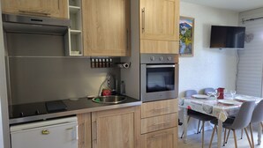 Una cuina compacta amb armaris de fusta, forn integrat, rentaplat i zona de menjador amb taula i cadires.