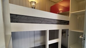 Habitació amb literes, un armari vermell i una porta blanca.