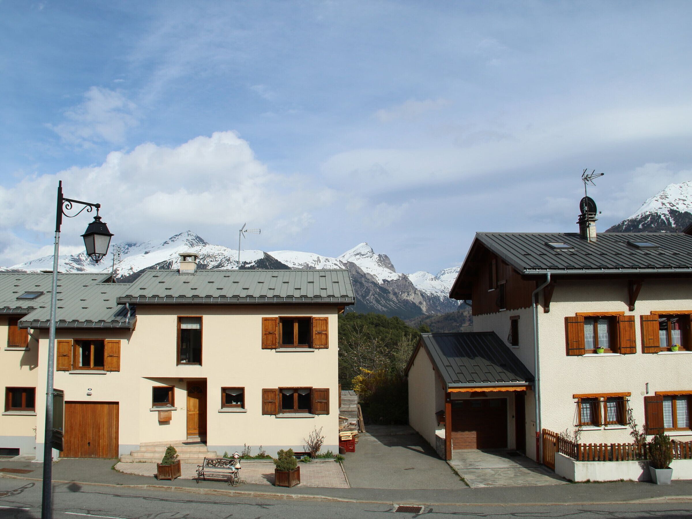 A row of traditional chalet-style buildings with wooden shutters, set against a backdrop of snow-capped mountains.