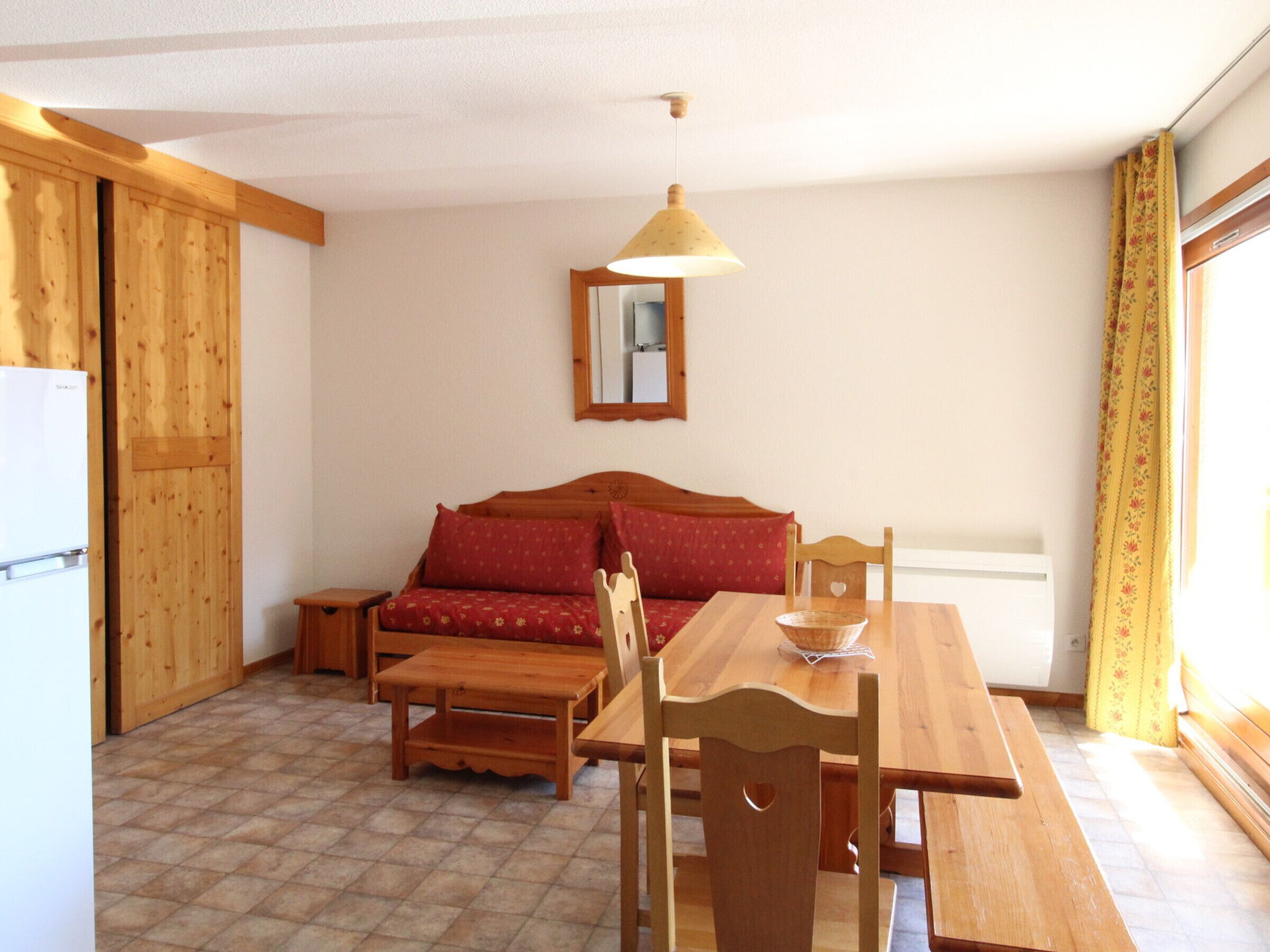 Een gezellige kamer met een houten bank, een eettafel met stoelen, een klein houten bijzettafeltje en een hanglamp.