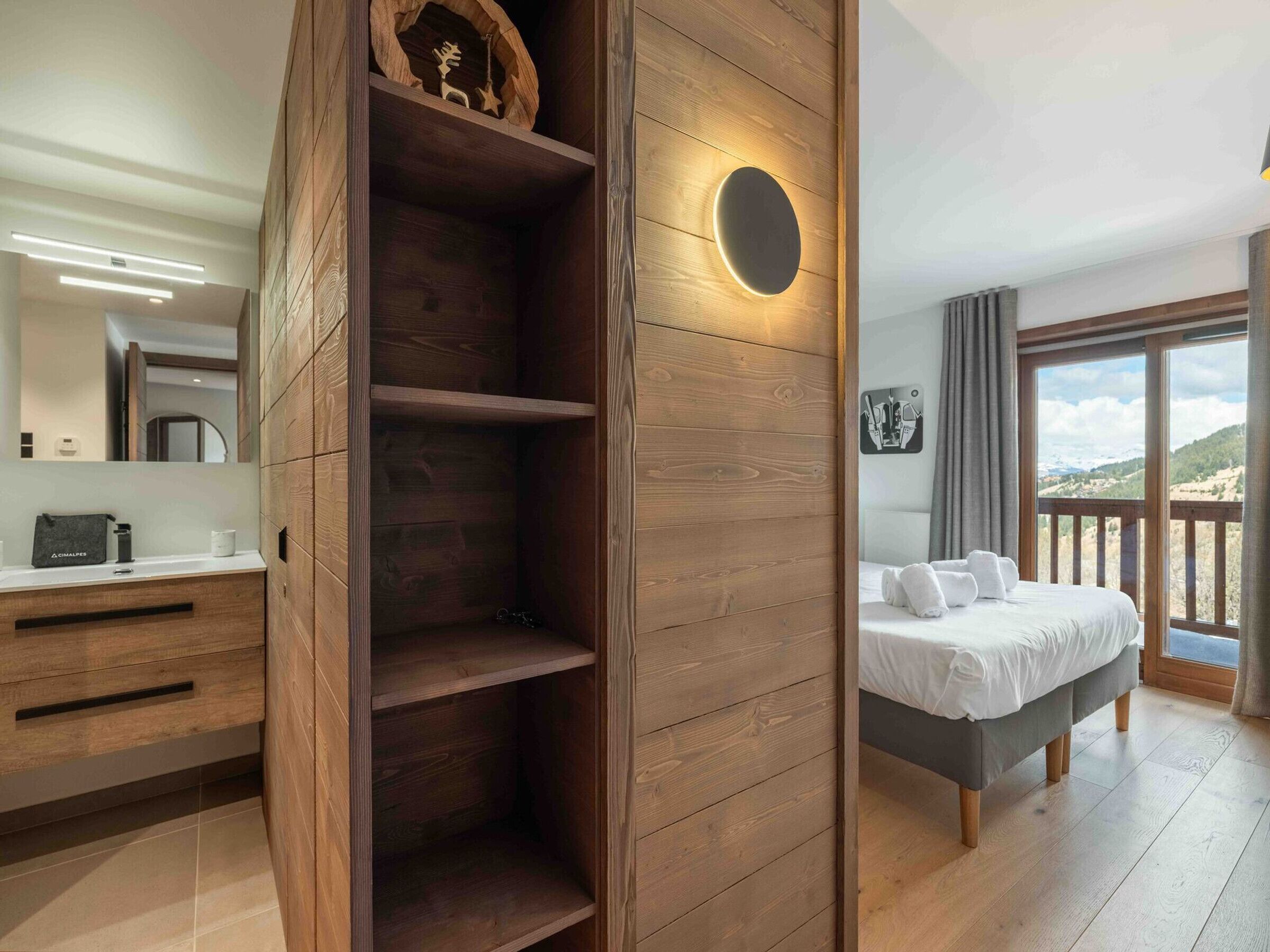 Een moderne hotelkamer met een houten garderobe, een bed met uitzicht en een badkamer met een spiegel en toiletartikelen.