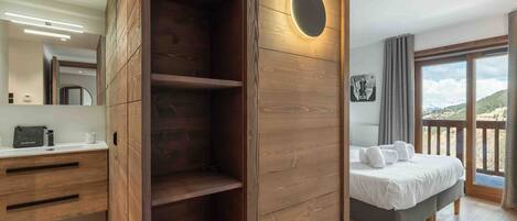 Een moderne hotelkamer met een houten garderobe, een bed met uitzicht en een badkamer met een spiegel en toiletartikelen.