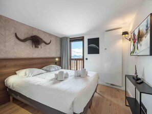 Quarto de hotel com uma cama grande, cabeceira de madeira, cabeça de animal montada, porta com vista e um quadro na parede.