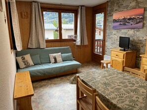 A cozy room with a wooden sofa, a small table, a chair, a television, and a painting on the wall.