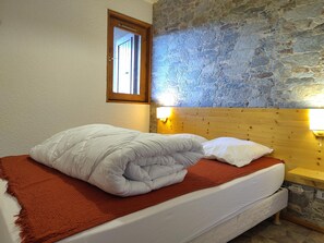 A bed with white bedding, a red throw blanket, and a wooden headboard.