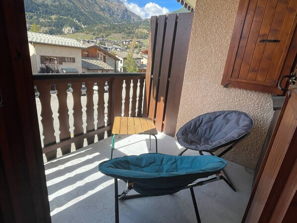 A balcony with a view of a mountain landscape, a folding chair, and a wooden fence.