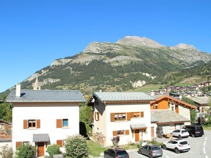 A mountain village with traditional chalet-style buildings, a parking area, and a clear view of the surrounding mountains.