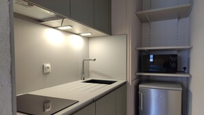 Eine kleine Küchenzeile mit integriertem Mikrowellenherd, Spüle mit Armatur und einer Arbeitsplatte mit einem Laptop.