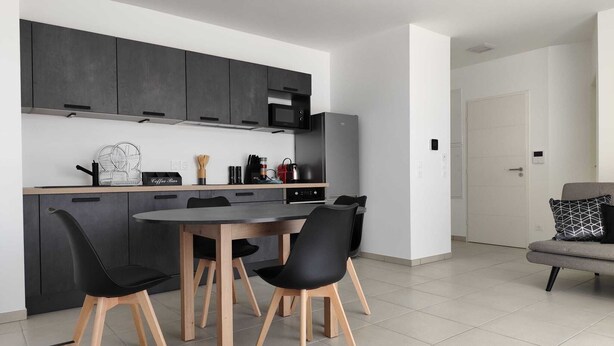 Une cuisine moderne avec des meubles de couleur sombre, un îlot central et un coin repas comprenant des chaises noires et une table en bois.