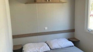 A bedroom with a bed, a wooden wardrobe, a nightstand, and a window. - Comfortable mobile home with terrace for 4 people (Argences-en-Aubrac)