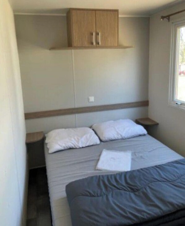 Un dormitorio con cama, armario de madera, mesita de noche y ventana.