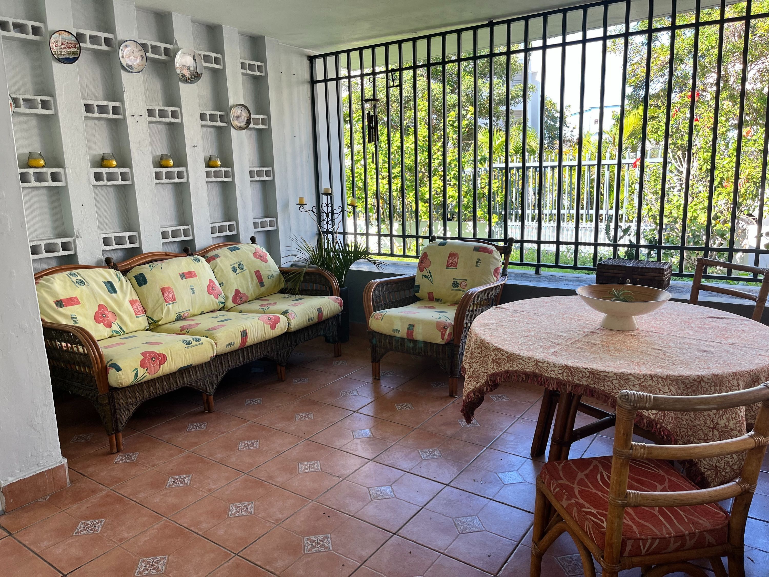 Un patio con sofá, sillas, una mesa y barandilla, con vistas a la vegetación.