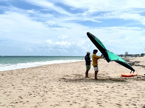 Two people on a sandy beach holding a large kite.