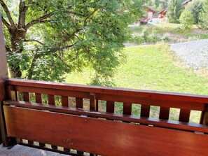 A wooden bench overlooking a grassy area with a tree and a building in the background.