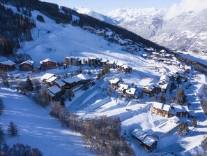 Une station de montagne enneigée, avec plusieurs bâtiments de style chalet, des pistes de ski et une vue dégagée sur les montagnes environnantes.