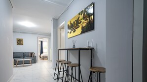 Un pasillo con zona de comedor que incluye una mesa, taburetes de bar, un sofá y un cuadro en la pared.