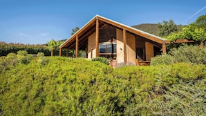 A modern house with a sloped roof, large windows, and a wooden deck. - Daybreak Lodge | High Country Earthen Escape (Tawonga)