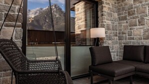 A stone-walled room with a swing chair and a sofa facing a large window overlooking mountains.