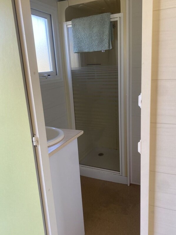 A bathroom with a shower, a sink, and a towel hanging on the door.