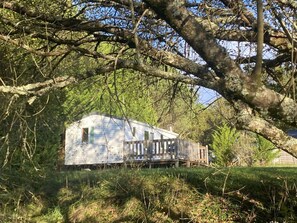 A mobile home with a fenced deck, surrounded by trees and grass.