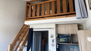 Una stanza in stile loft con un balcone in legno, una scala e un'apertura che dà su un'altra stanza.