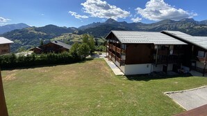 Un rifugio di montagna con facciata in legno e un balcone, immerso nel verde e con montagne sullo sfondo.