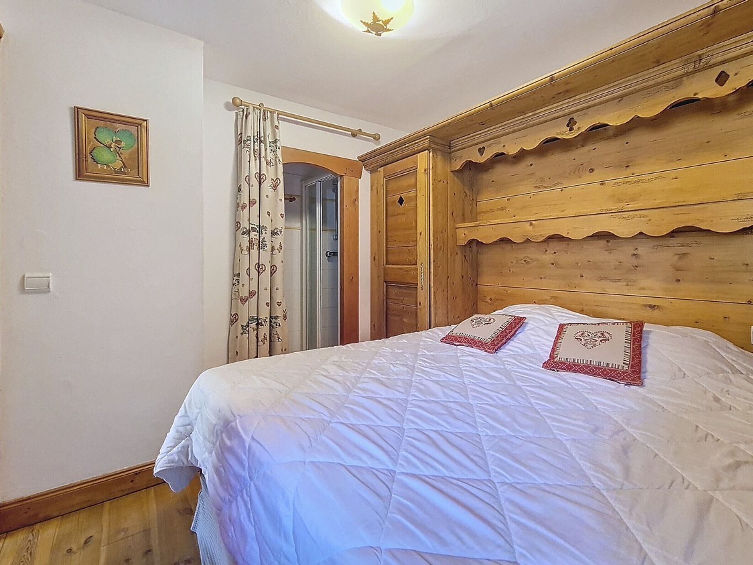 A bedroom with a wooden headboard, a bed with white bedding, a door leading to a bathroom, and a wall-mounted light fixture.