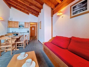 A cozy room with a wooden ceiling, a red sofa, a dining table with chairs, and a kitchen area in the background. - Les Menuires - 3 rooms, 6 guests, southwest balcony (Les Menuires)
