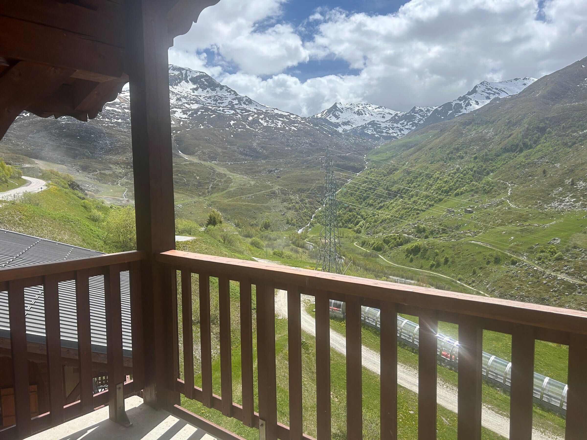 Een balkon met uitzicht op een bergachtig landschap, inclusief besneeuwde toppen en een vallei met een kronkelende weg.
