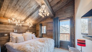 Ein gemütliches Schlafzimmer mit einem großen Bett, Holzbalkendecke und Blick auf Berge durch ein Fenster.