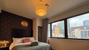 Een hotelkamer met een groot bed, uitzicht op de stad, een ronde spiegel aan de muur en een kroonluchter.