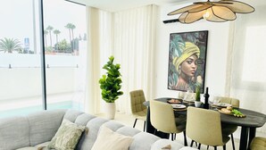 A modern dining area with a round table, chairs, and a large window offering a view of palm trees and a building. - Casa Sirocco by At Home Costa del Sol (Nerja)