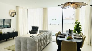 A modern living room with a sectional sofa, a dining table set for four, and a large window with curtains. - Casa Sirocco by At Home Costa del Sol (Nerja)
