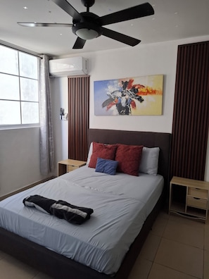Una camera d'albergo moderna con un letto, una ventola a soffitto, un quadro e una finestra con tende.