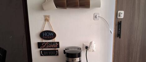 Eine Kaffeemaschine auf einem weißen Schrank, ein Wandregal mit Kaffeetassen und ein Schild mit der Aufschrift 'Coffee'.