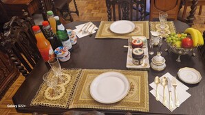 Een eettafel gedekt met borden, bestek en een schaal fruit.
