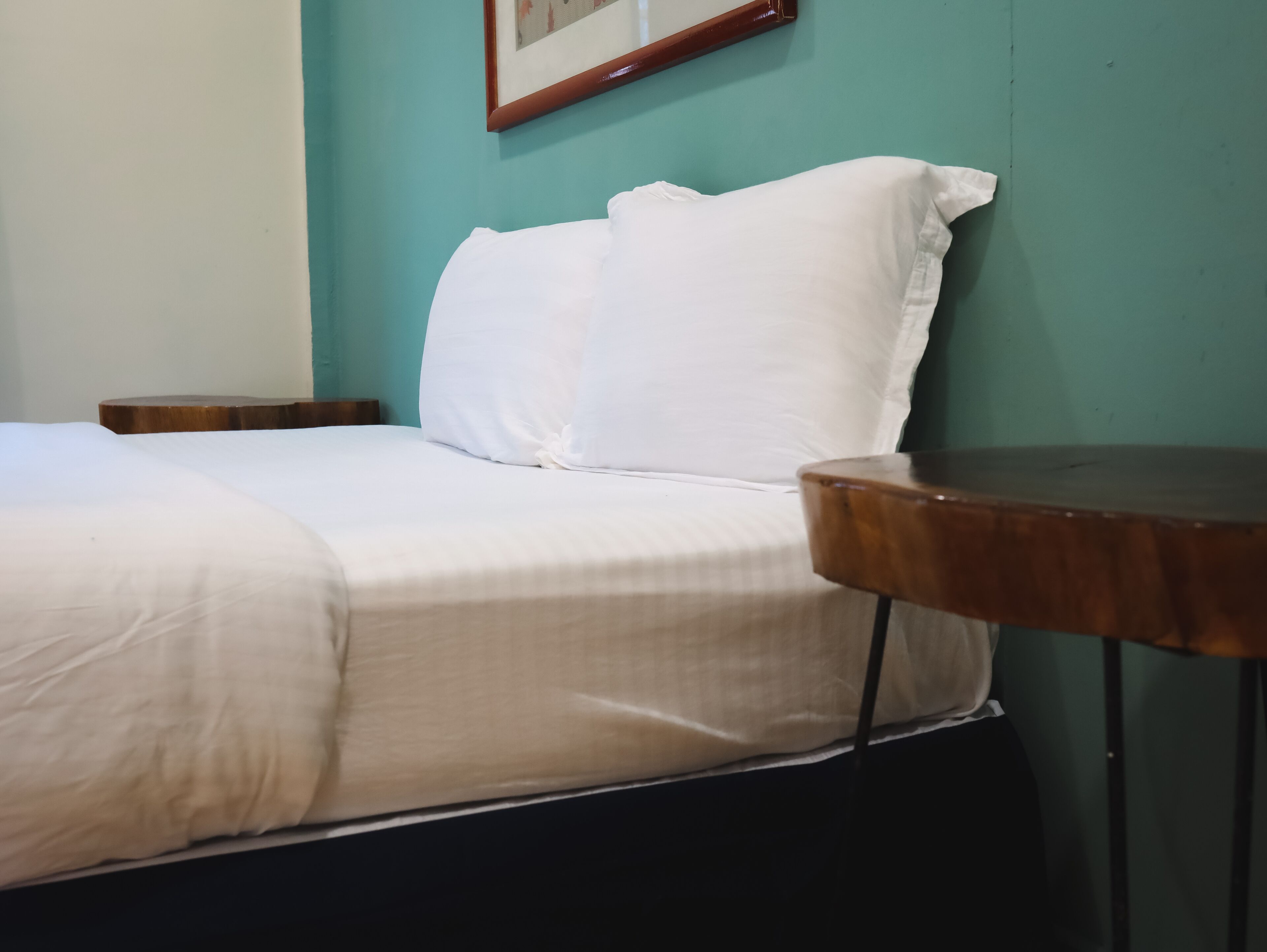 Uma cama com roupa de cama branca, uma mesa de cabeceira de madeira e uma pequena mesa com tampo de madeira.