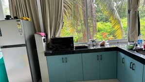 A kitchen with teal cabinets, a refrigerator, and a window with curtains. - The Tranquo Stays (Alibag)